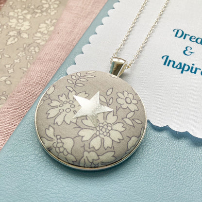 Grey Liberty floral necklace with a star design on a blue book
