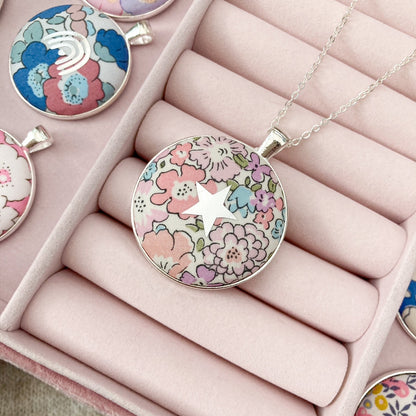 Floral pendant necklace on display with other pendants in a pink jewelry box.