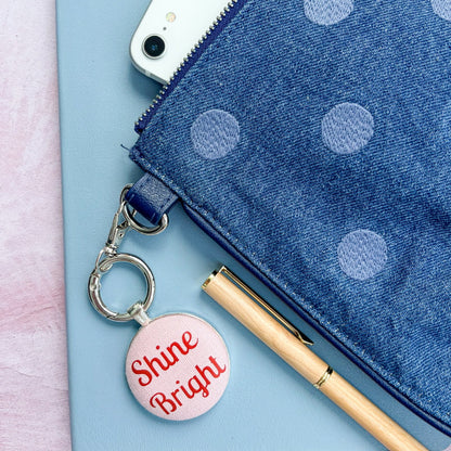 Blue polka dot pouch with a "Shine Bright" red and pink keyring on a light pink background