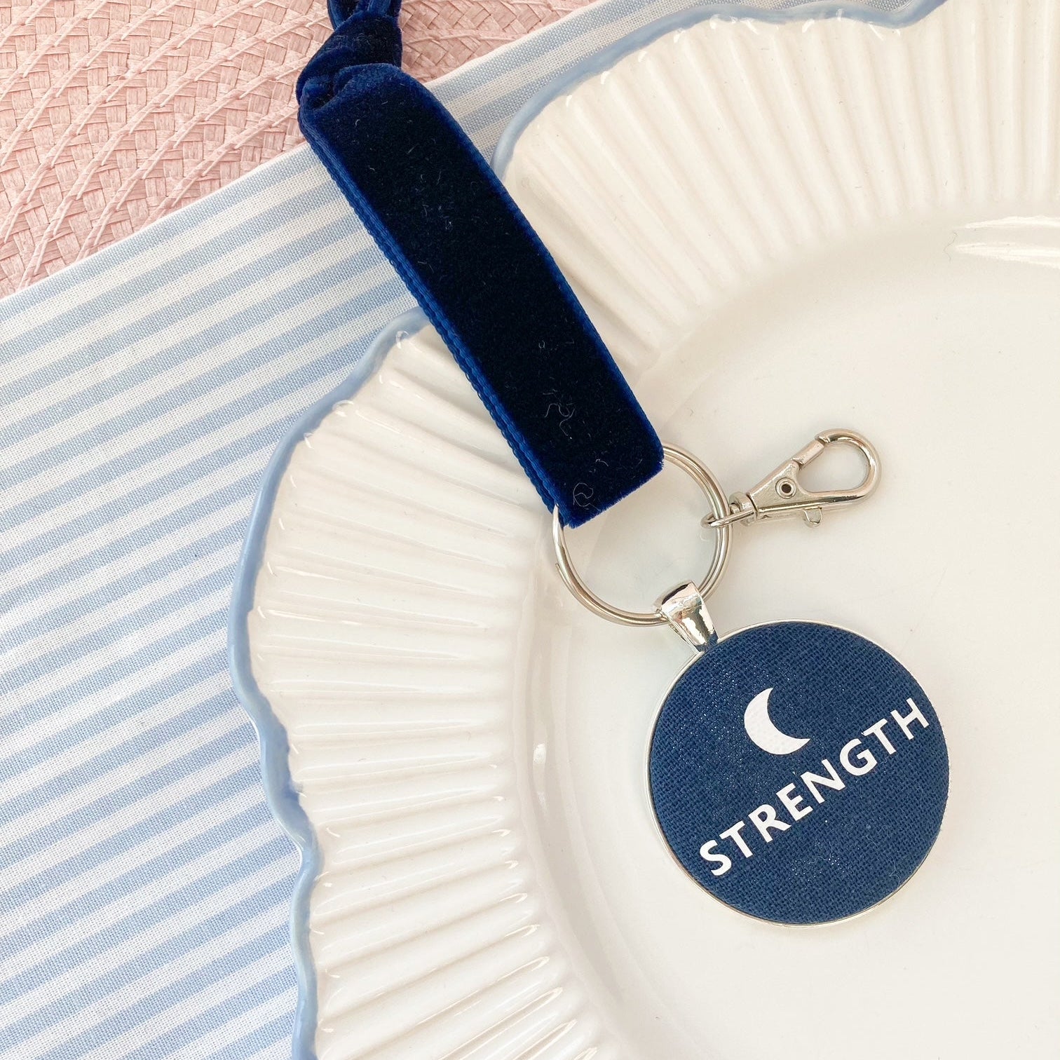 Keychain with 'STRENGTH' and a crescent on a navy blue fabric, on a white plate