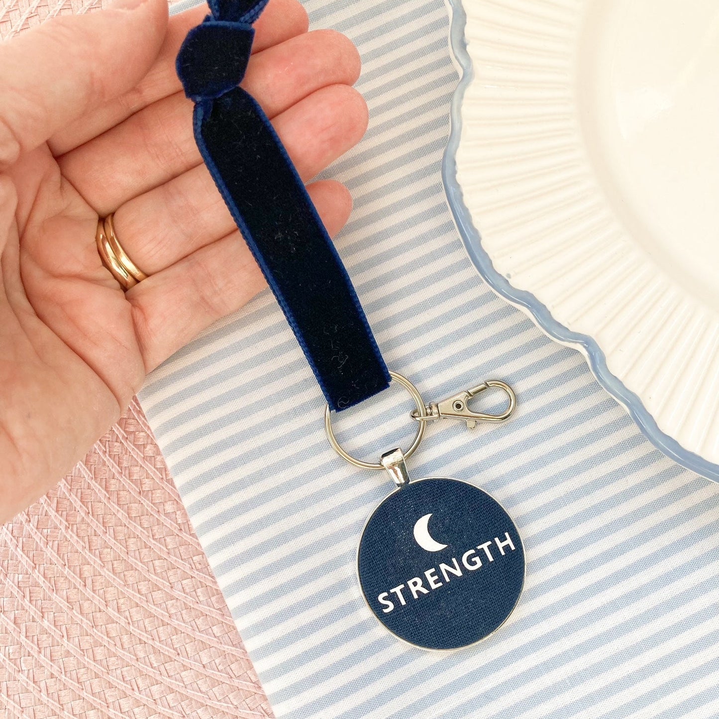 Navy blue keepsake with 'STRENGTH' and a new moon design held by a hand on a striped background