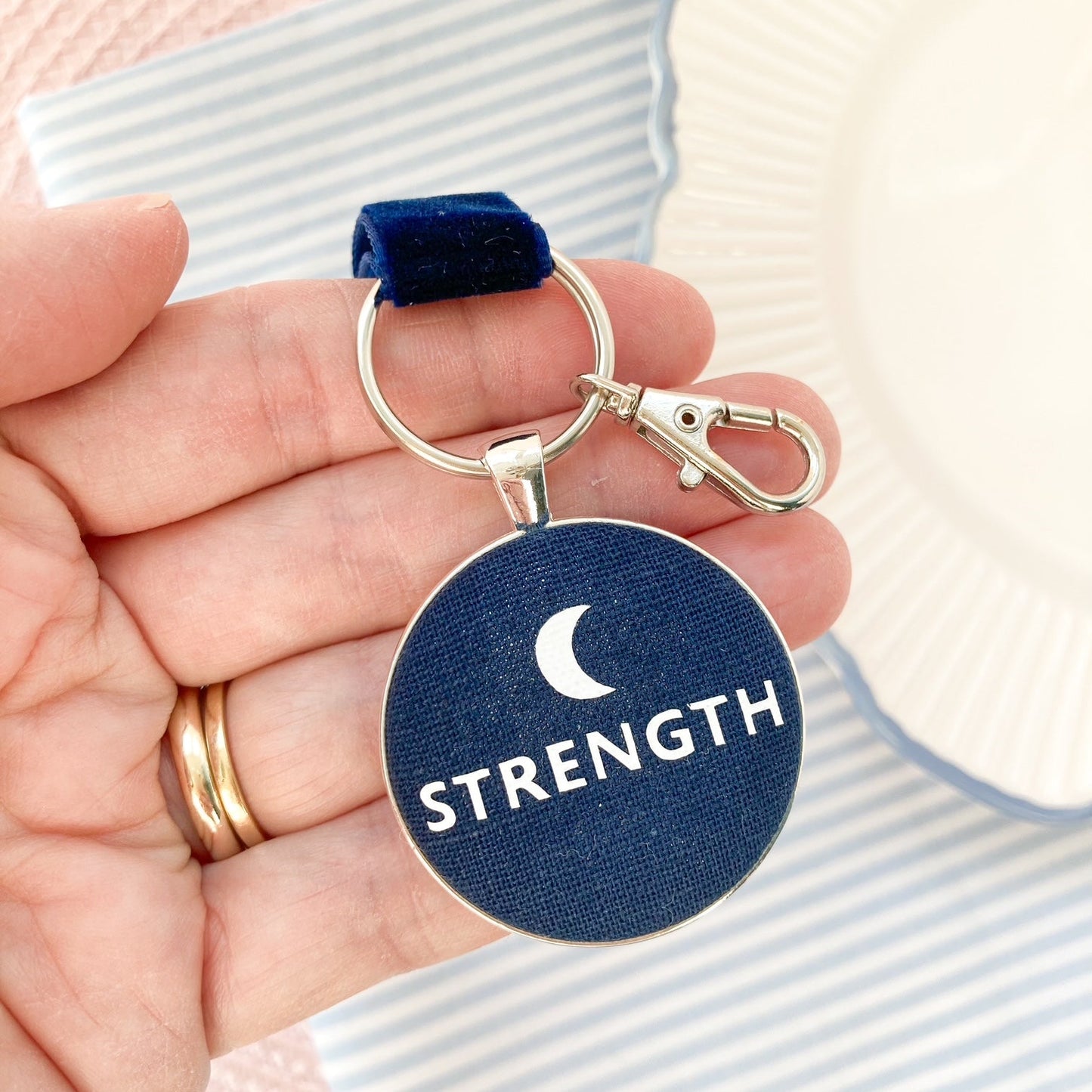 Key ring with 'STRENGTH' and moon symbol, held in a hand.