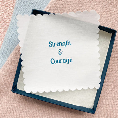 Fabric message with 'Strength & Courage' text in a blue gift box on a textured surface