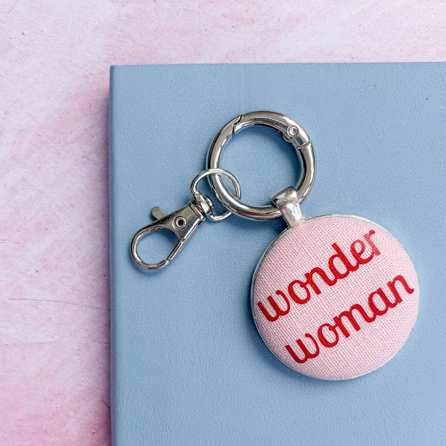 Keyring with 'wonder woman' text printed in red on pink fabric, on a pink and blue background
