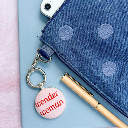 Pink 'wonder woman' bag charm on a blue polka dot pouch with a phone and pen.