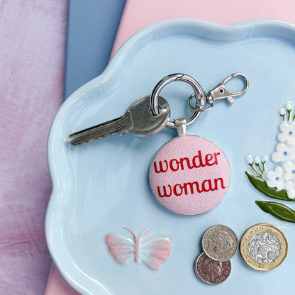 Keyring with red and pink 'wonder woman' charm on a light blue dish with coins and flowers.