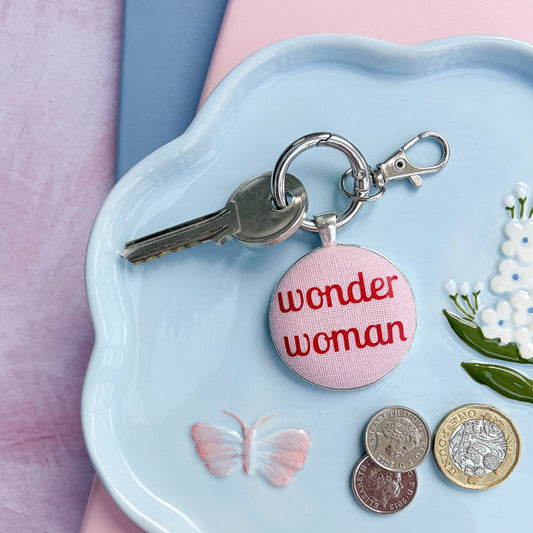 Keyring with red and pink 'wonder woman' charm on a light blue dish with coins and flowers.