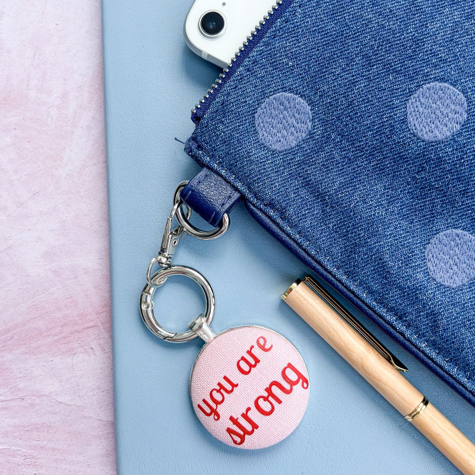 Keyring and bag charm with 'you are strong' message, on a polka dot bag and notebook