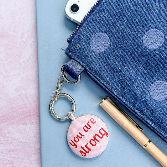 Keyring and bag charm with 'you are strong' message, on a polka dot bag and notebook