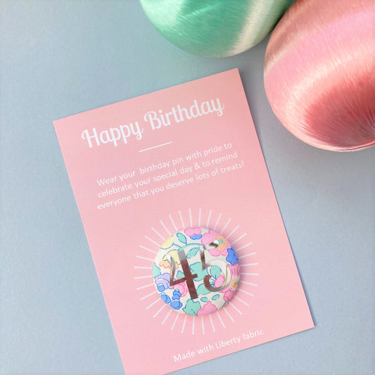 A fabric pink floral birthday badge printed with the number 45 in silver foil, on a Happy birthday postcard.