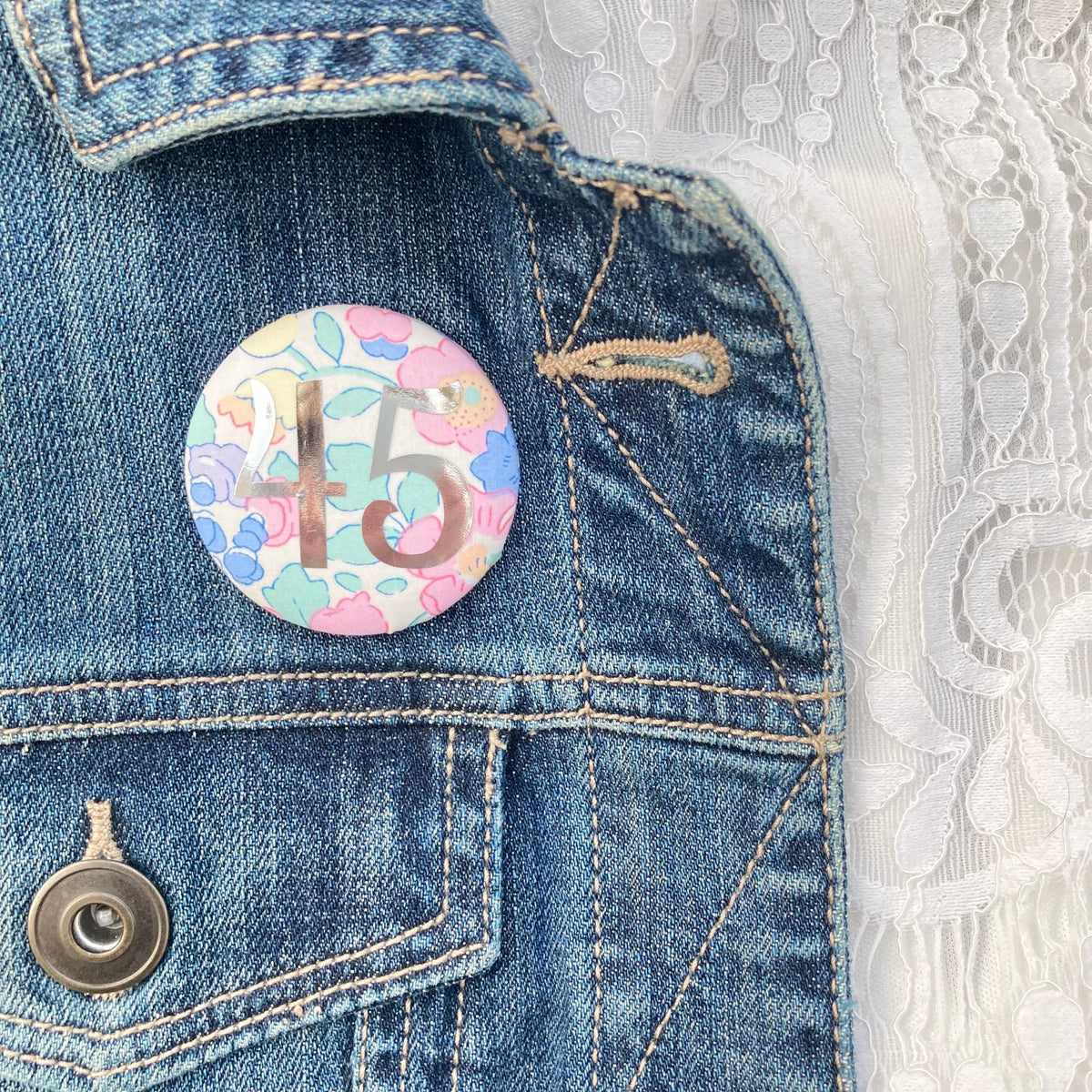A fabric pink floral birthday badge printed with the number 45 in silver foil, on a Happy birthday postcard.