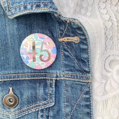 A fabric pink floral birthday badge printed with the number 45 in silver foil, on a Happy birthday postcard.