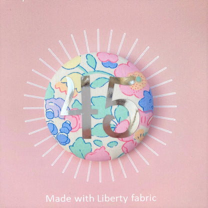 A fabric pink floral birthday badge printed with the number 45 in silver foil, on a Happy birthday postcard.