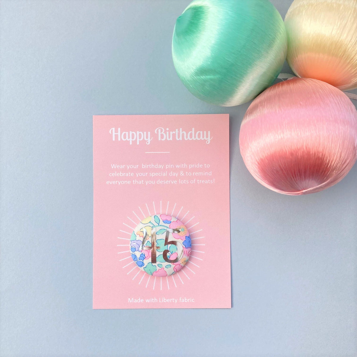 A fabric pink floral birthday badge printed with the number 45 in silver foil, on a Happy birthday postcard.