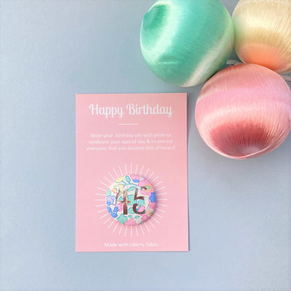 A fabric pink floral birthday badge printed with the number 45 in silver foil, on a Happy birthday postcard.
