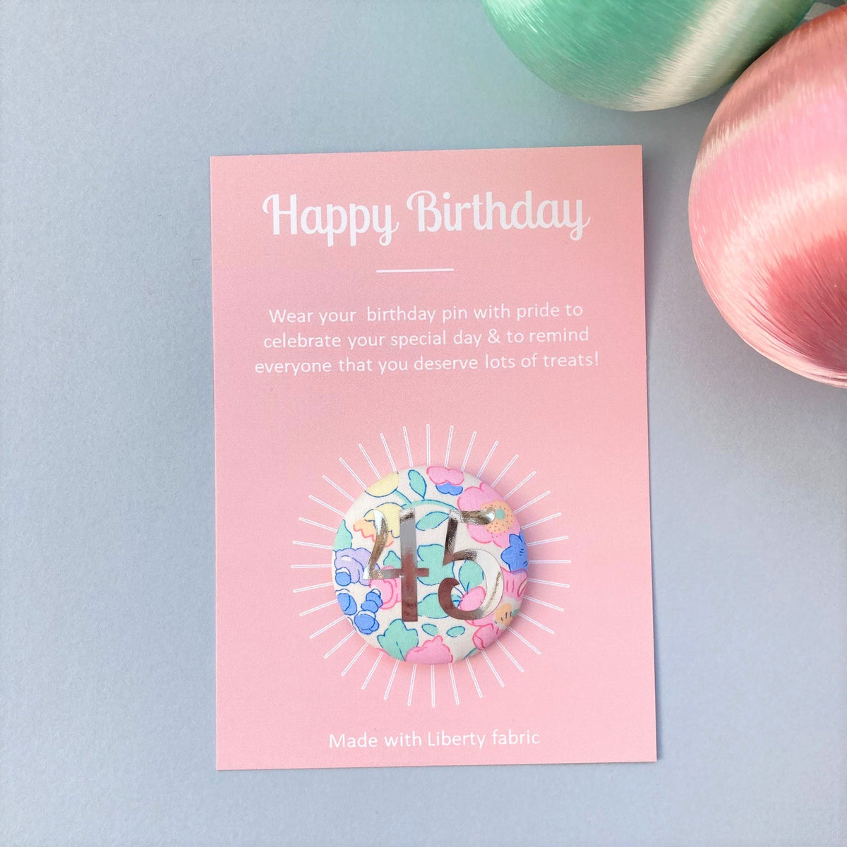 A fabric pink floral birthday badge printed with the number 45 in silver foil, on a Happy birthday postcard.