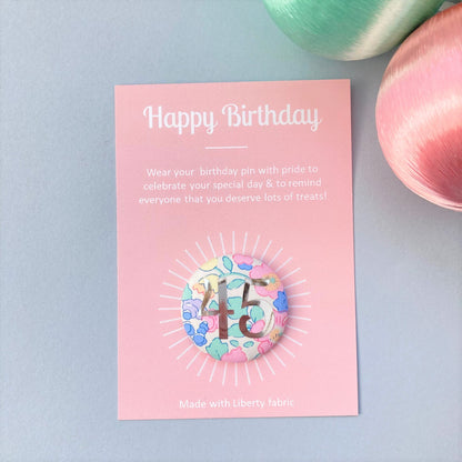 A fabric pink floral birthday badge printed with the number 45 in silver foil, on a Happy birthday postcard.