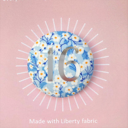 A round birthday pin with blue floral pattern and the number 16 in silver foil, indicating it is suitable for a 16th birthday.