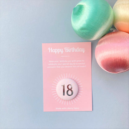 A fabric pale pink '18' birthday pin with a silver plated brooch fastening, attached to a birthday postcard