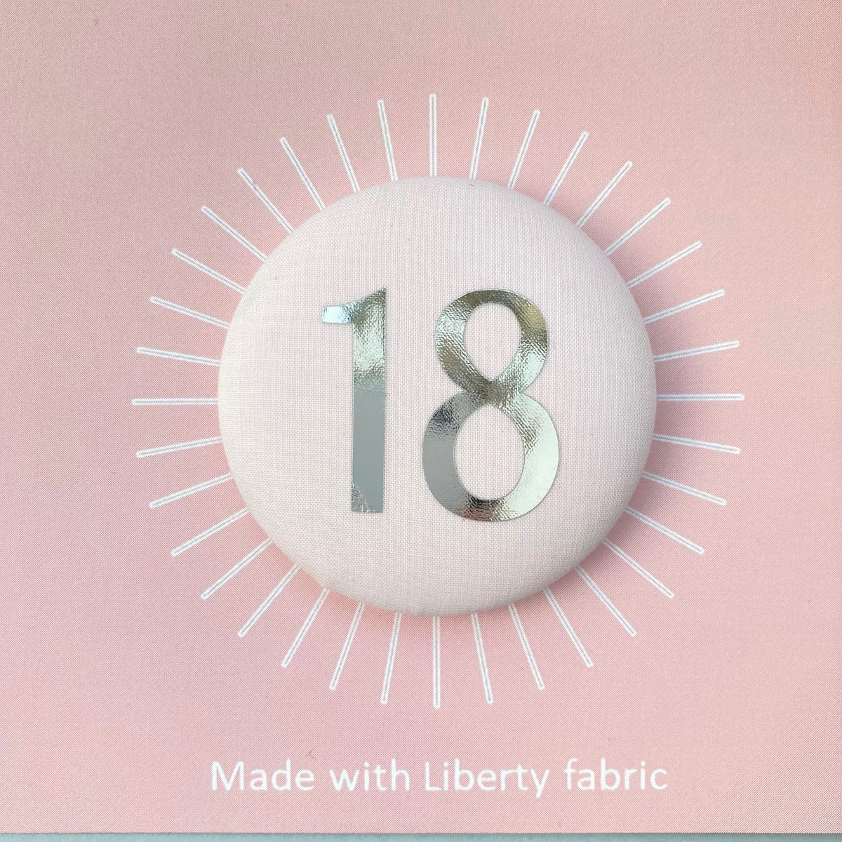 A fabric pale pink '18' birthday pin with a silver plated brooch fastening, attached to a birthday postcard
