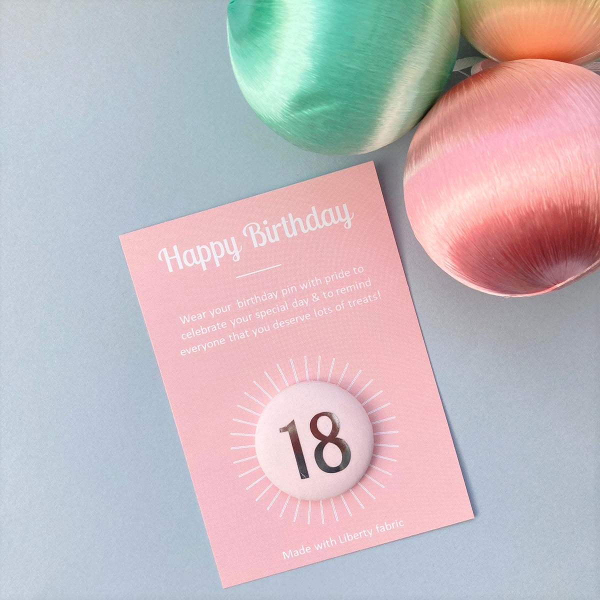 A fabric pale pink '18' birthday pin with a silver plated brooch fastening, attached to a birthday postcard